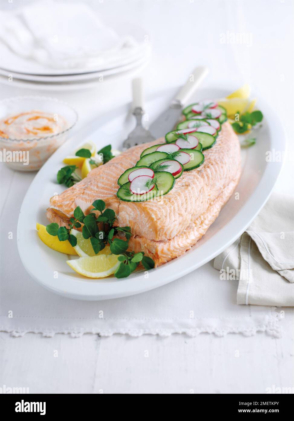 Whole poached salmon garnished with slices of cucumber, radish, watercress and lemon wedges, served with chilli mayonnaise Stock Photo