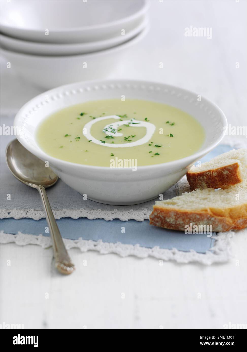 Leek and potato soup garnished with swirl of cream and herbs, served with bread Stock Photo