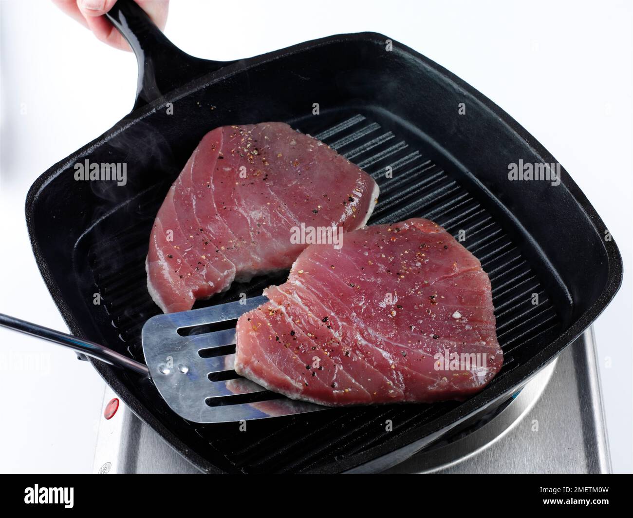 Chargrilling tuna steaks in pan, using spatula to turn over the steaks