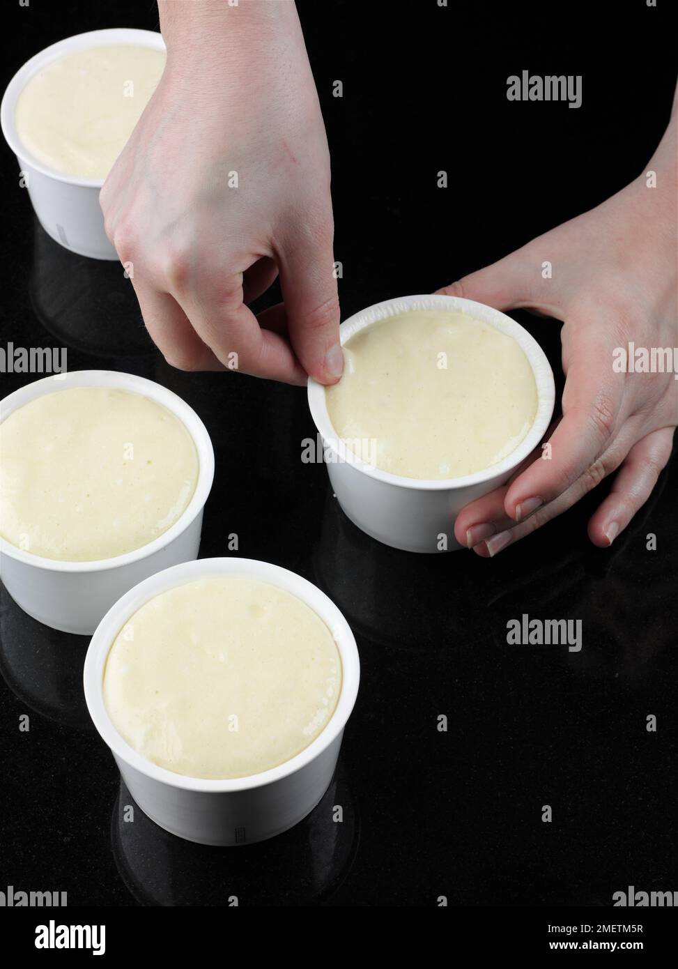 Making cheese souffles, woman running thumb nail around the inside rim of ramekin to prevent the souffle catching the sides Stock Photo