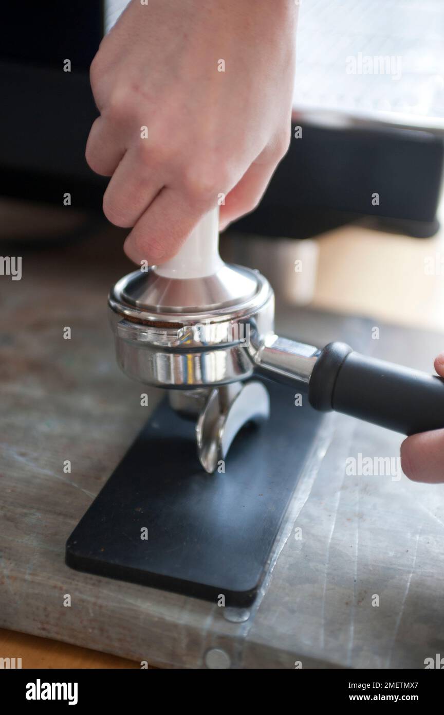 Using tamper to push down coffee grinds in basket of portafilter Stock ...