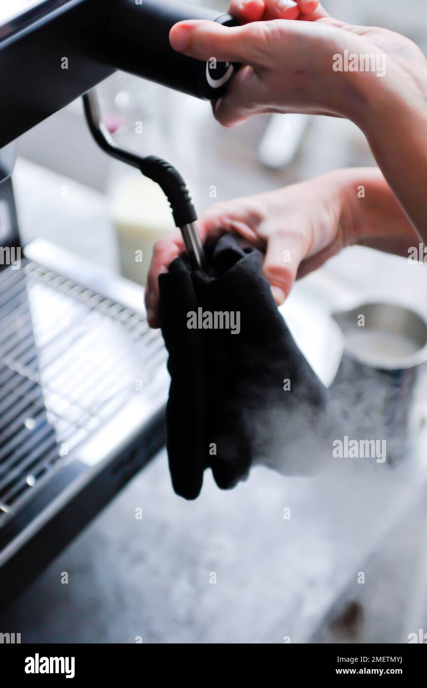 Using damp cloth to clean steam wand on espresso machine Stock Photo