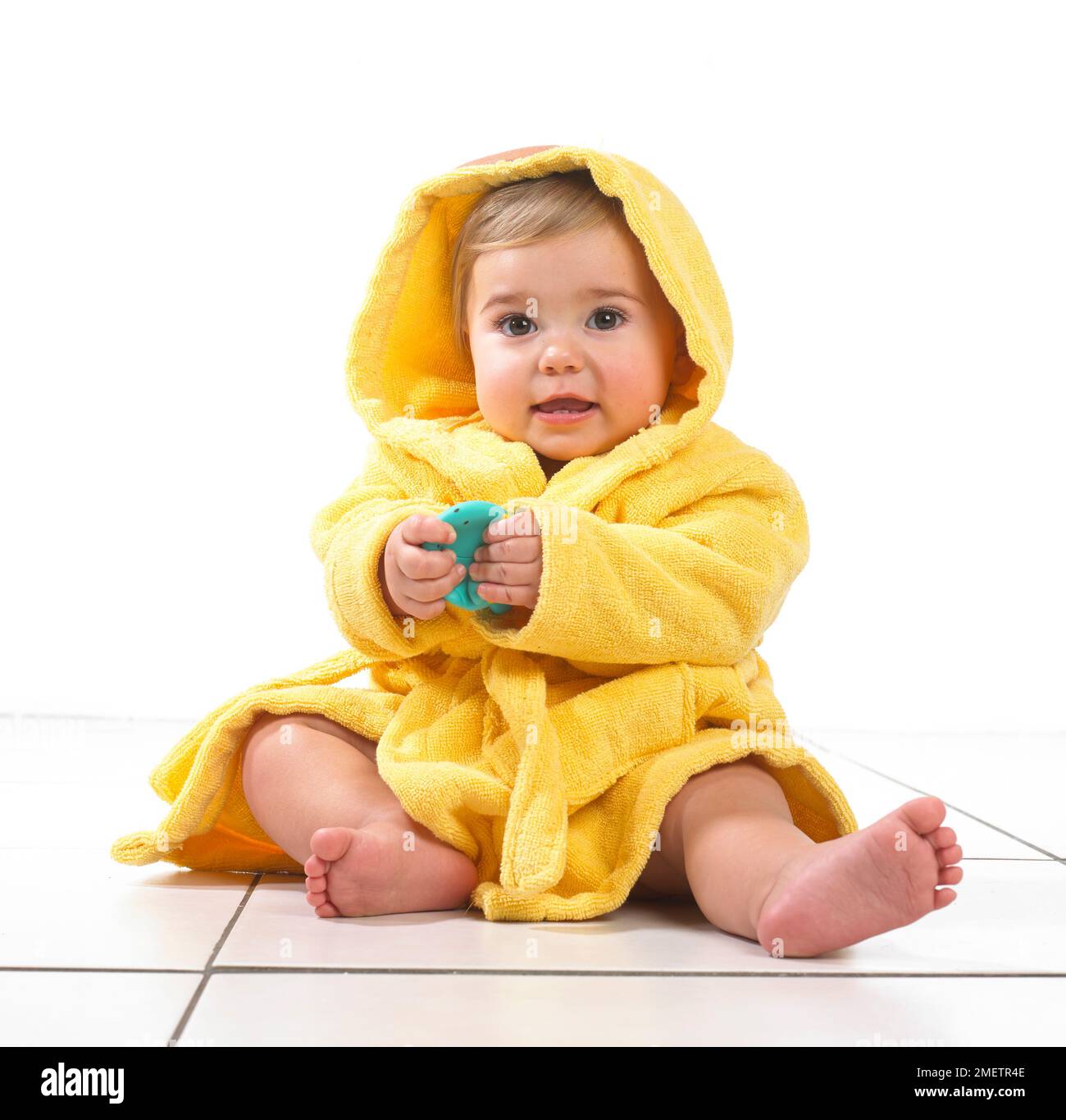 Baby girl sitting wearing yellow dressing gown, 12 months Stock Photo