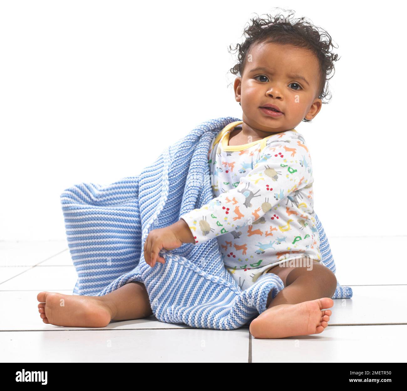 Girl sitting holding a kitted blanket around her, 18 months Stock Photo