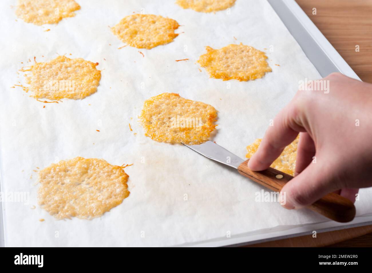 Making Parmesan crisps, lifting baked crisps of sheet with palette knife Stock Photo