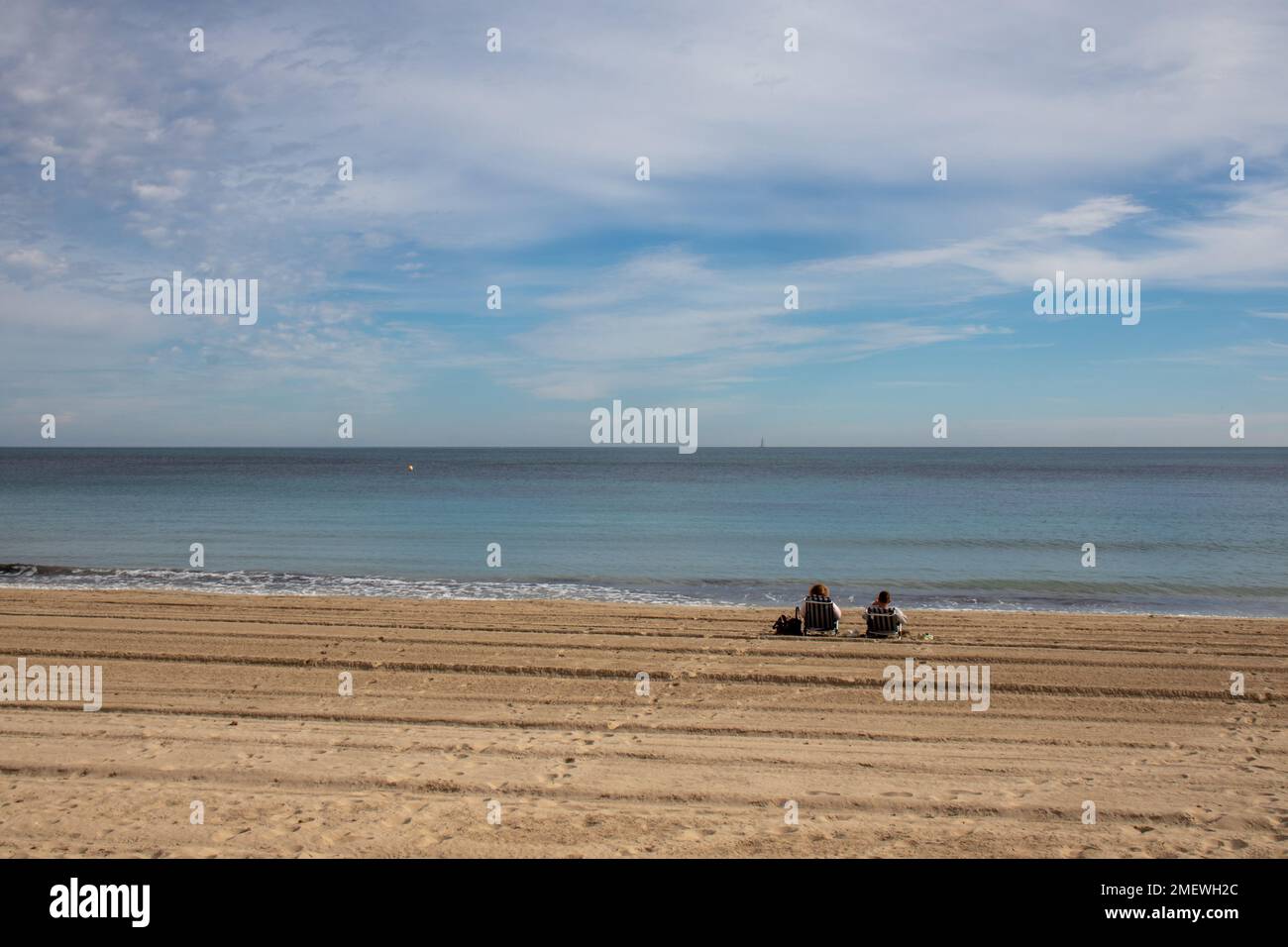 Pareja sentada en una playa frente al mar en invierno, España Stock Photo