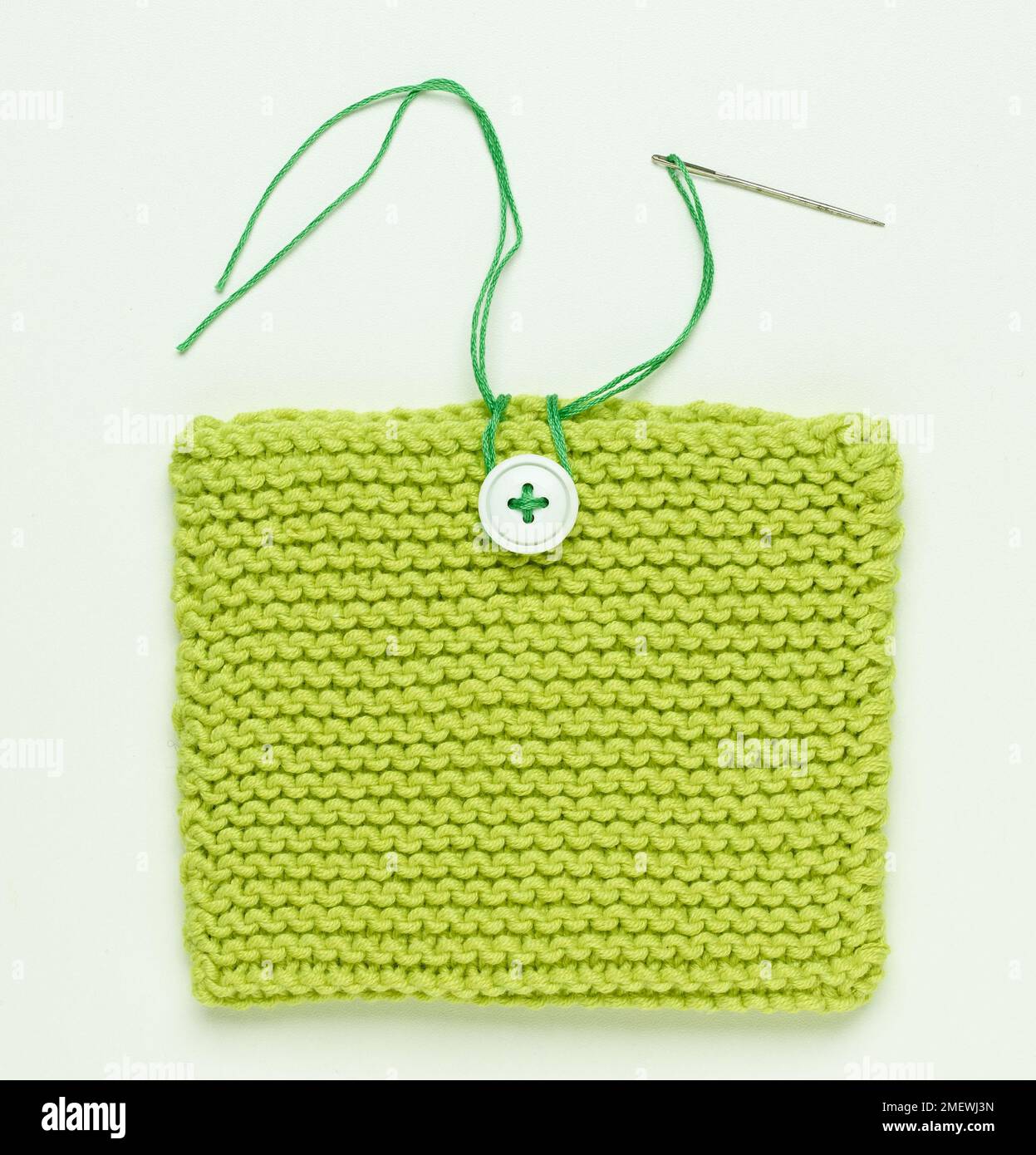 Steps for making knitted bag in green yarn, with button fastening, long green ribbon handles, and ribbon trim. Stock Photo