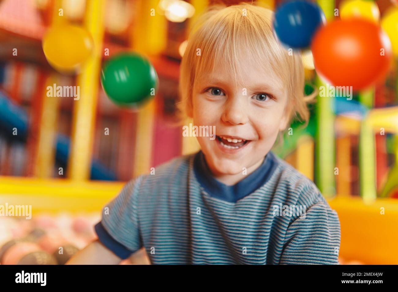Happy little boy playing in amusement park balls pool. Child throwing
