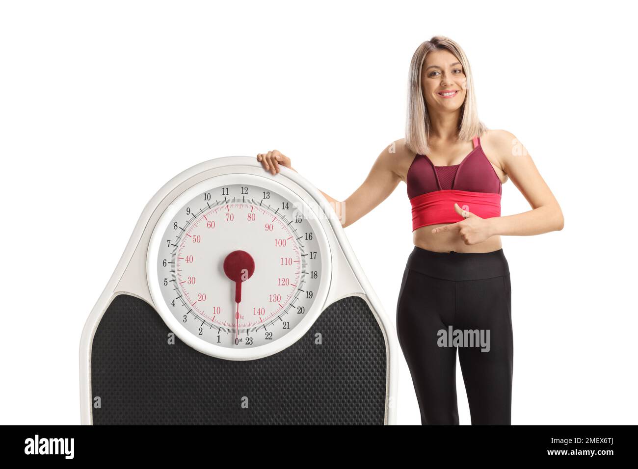 Young sporty woman leaning on a big weight scale and pointing isolated on white background Stock Photo