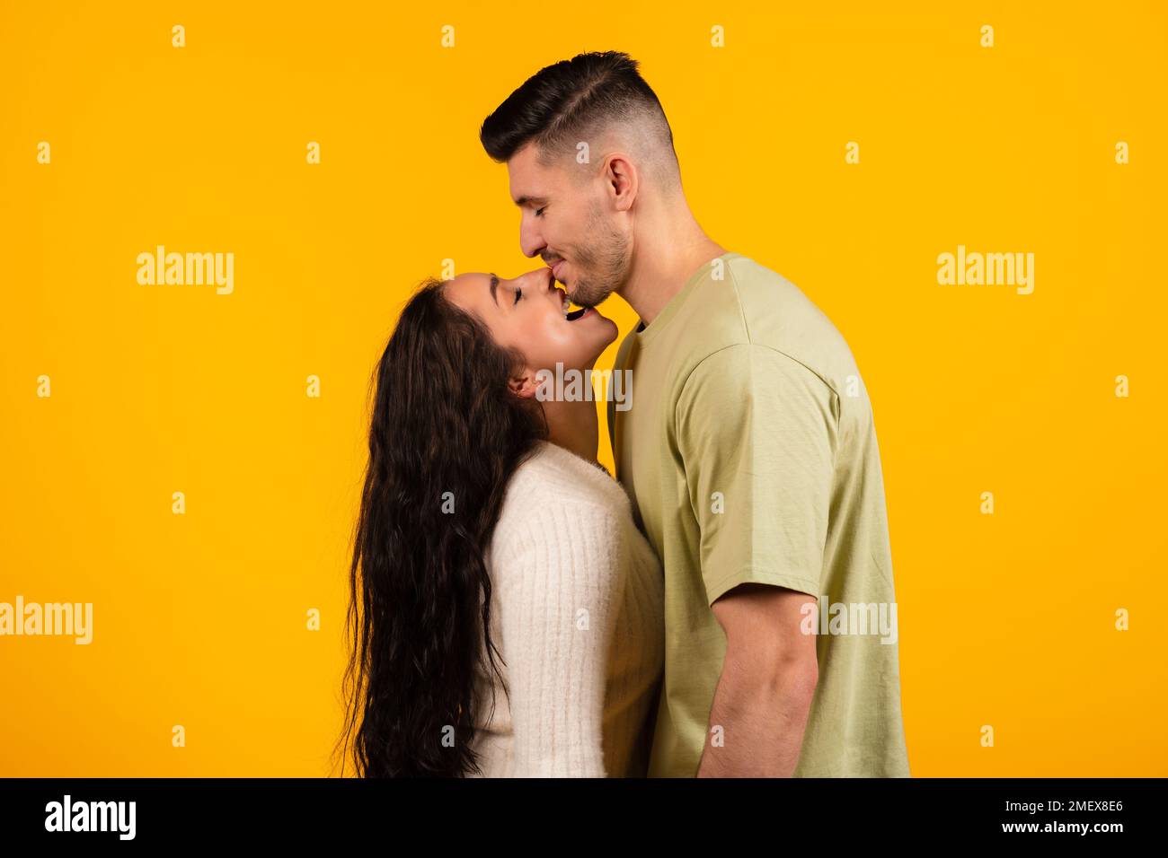 Glad smiling millennial arabic wife biting tall husband in chin, couple enjoy free time and have fun Stock Photo