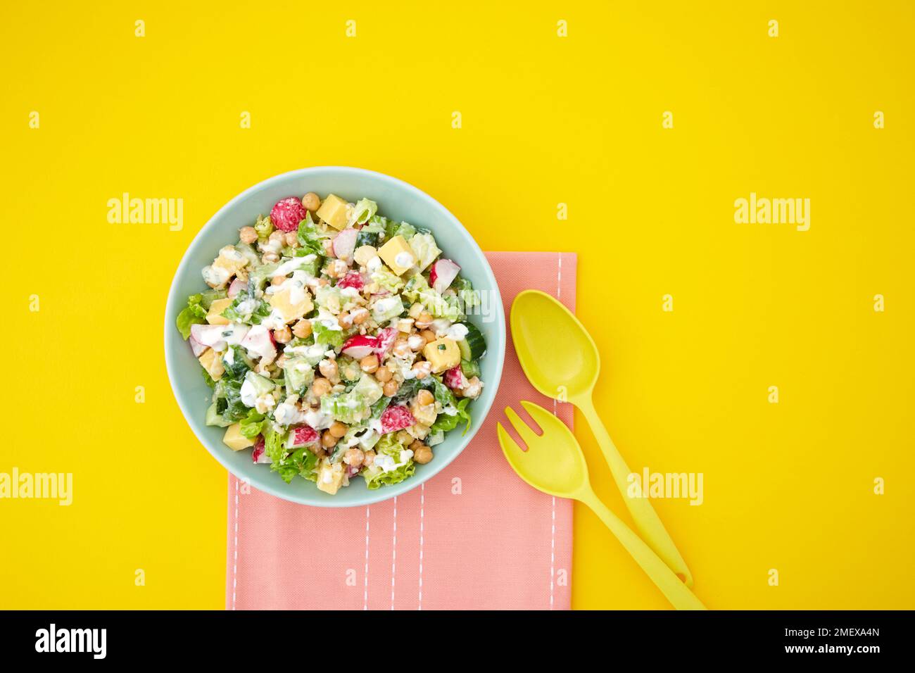 Chopped salad arranged overhead on yellow background with salad servers Stock Photo