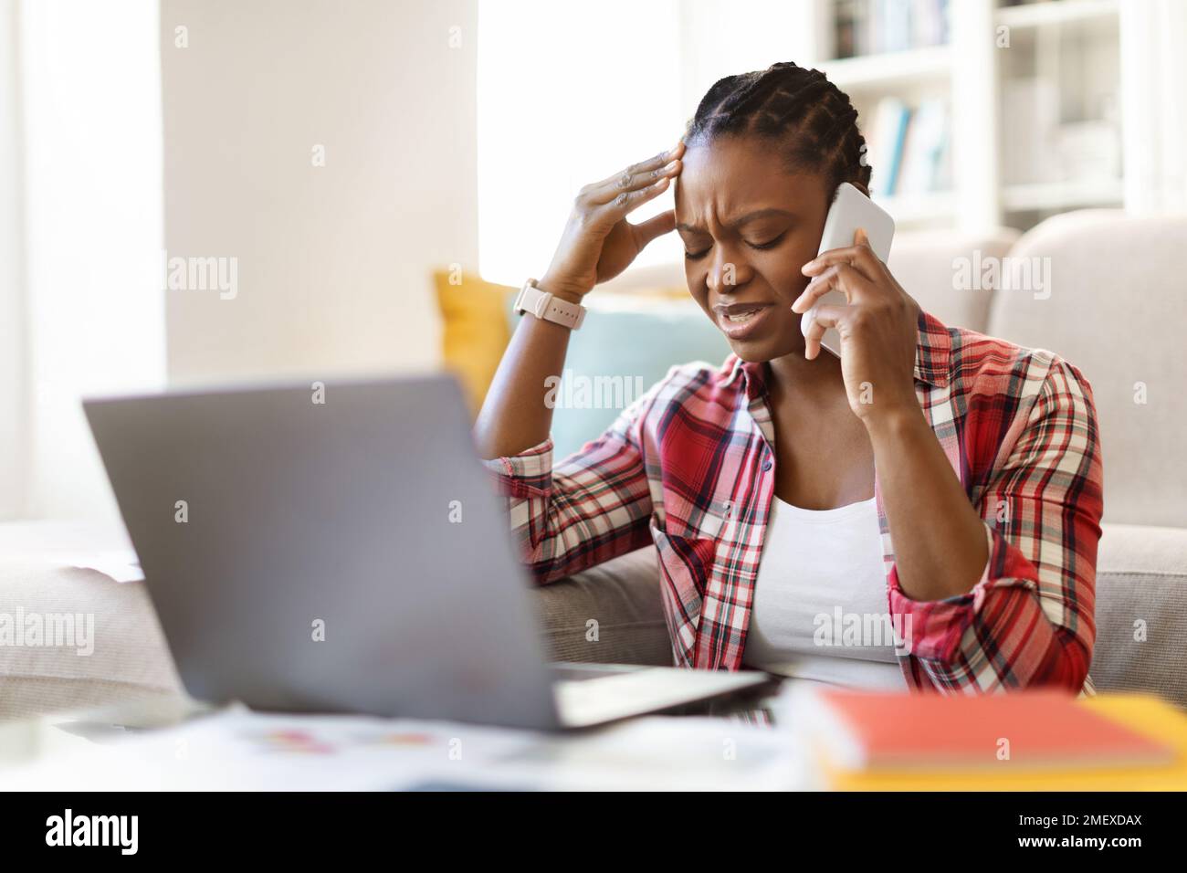 Depressed upset african female sit at workplace, using computer, phone Stock Photo