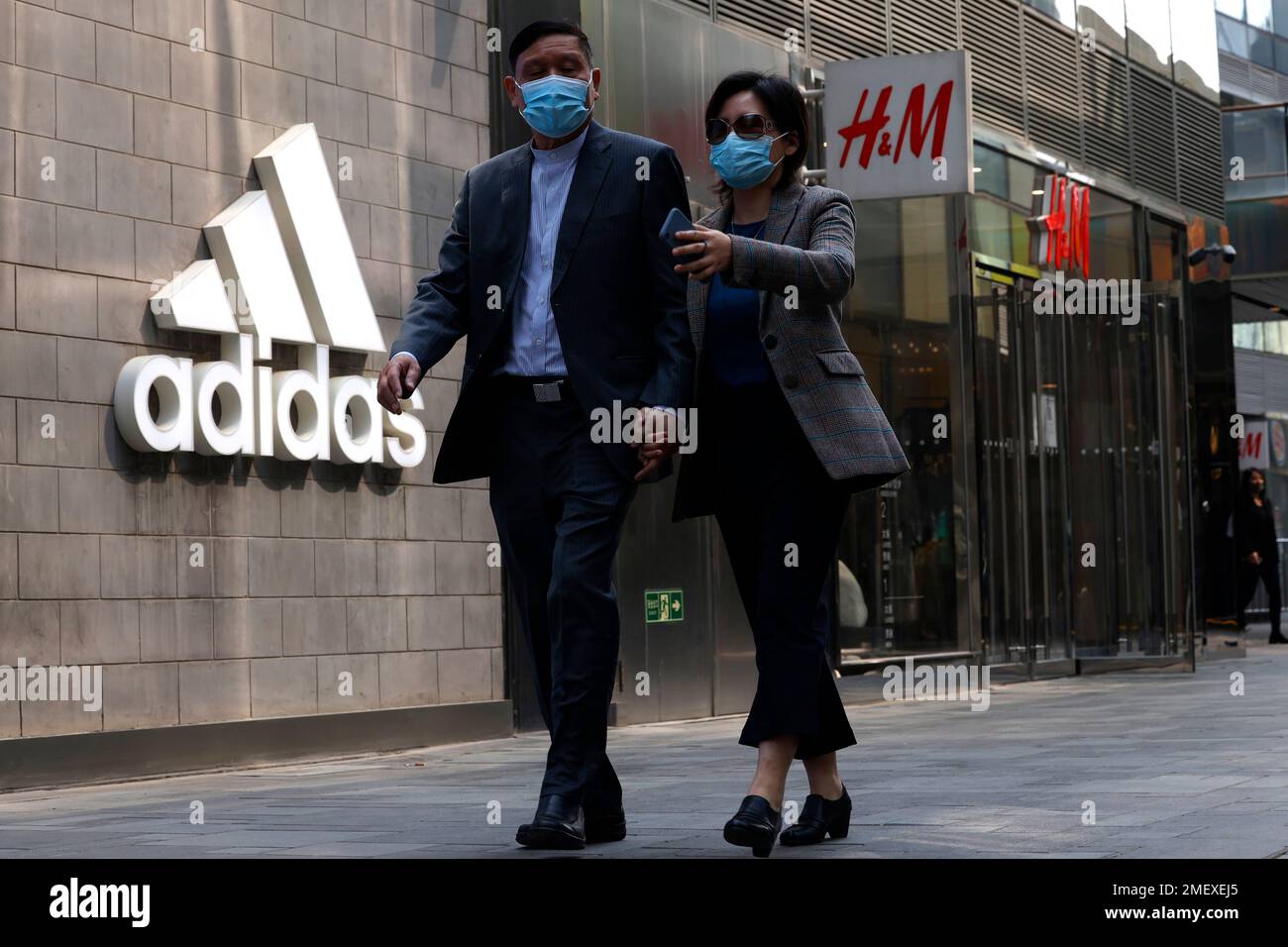 Visitors to a mall shopping area pass by Adidas and H&M stores in Beijing,  Thursday, March 25, 2021. China's ruling Communist Party is lashing out at  H&M and other clothing and footwear