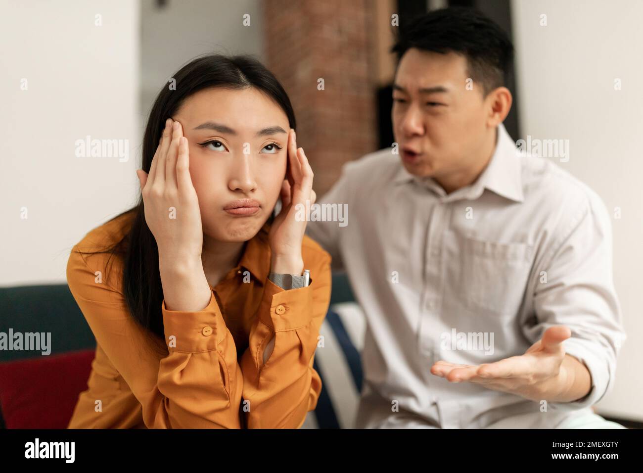 Emotional japanese mature man gesturing and shouting at his wife, chinese couple having quarrel at home Stock Photo