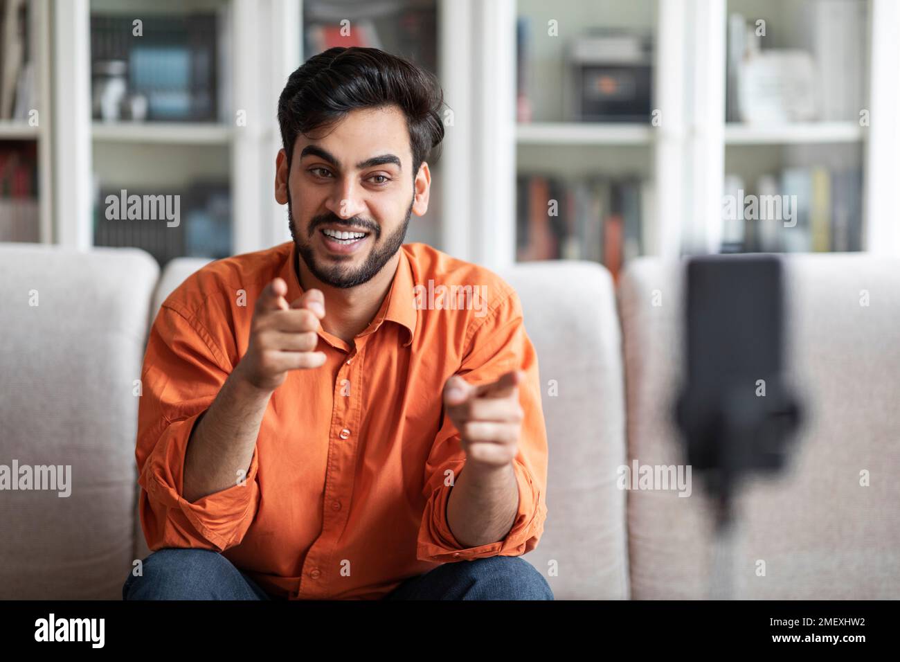Arab guy vlogger streaming from home, using phone on tripod Stock Photo