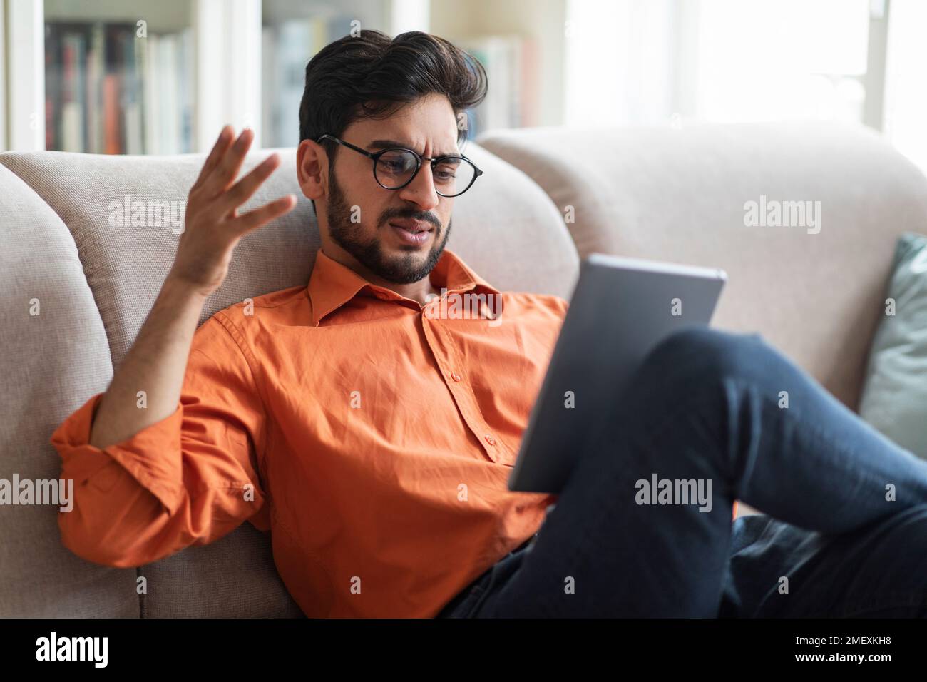 Angry middle eastern man sitting on couch, using digital pad Stock Photo