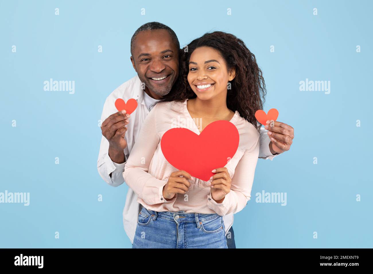 Love is in the air. Portrait of romantic black couple with red paper hearts in hands posing over blue background Stock Photo
