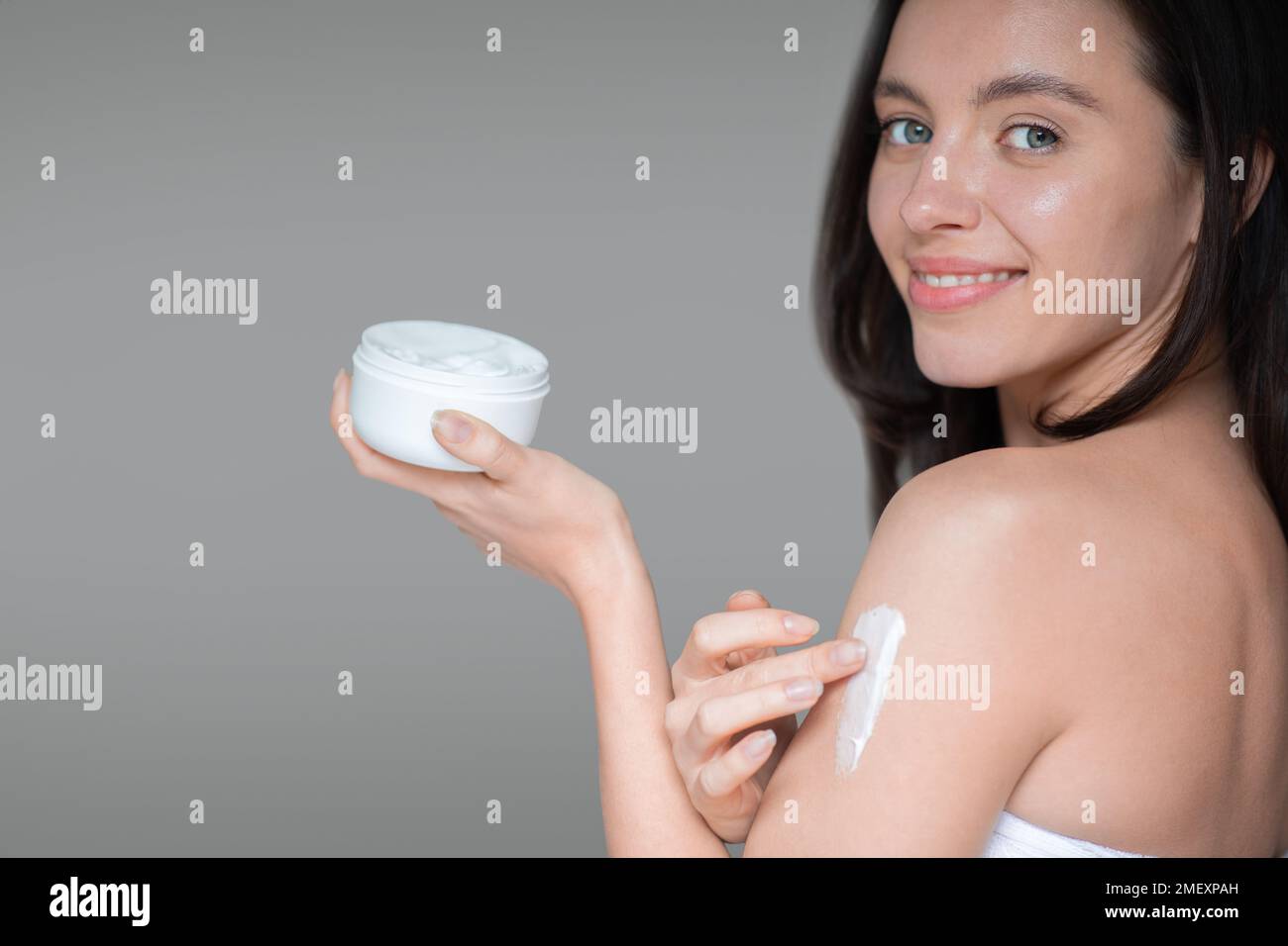Smiling young european woman without makeup with natural beauty applies cream on shoulder, holds jar Stock Photo