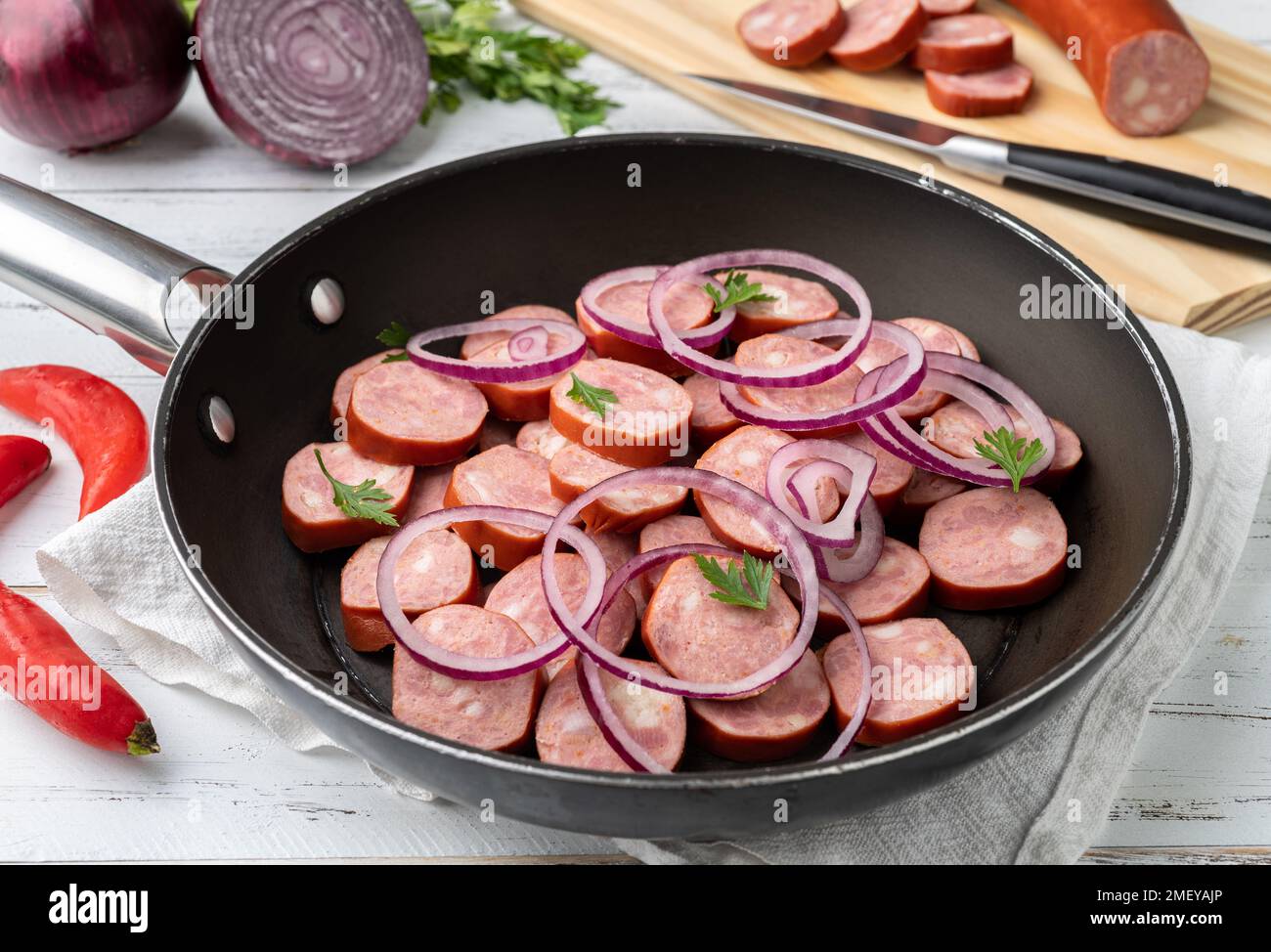Uncooked calabrese sausage slices in a pan with onion, pepper and herbs over white wooden table. Stock Photo