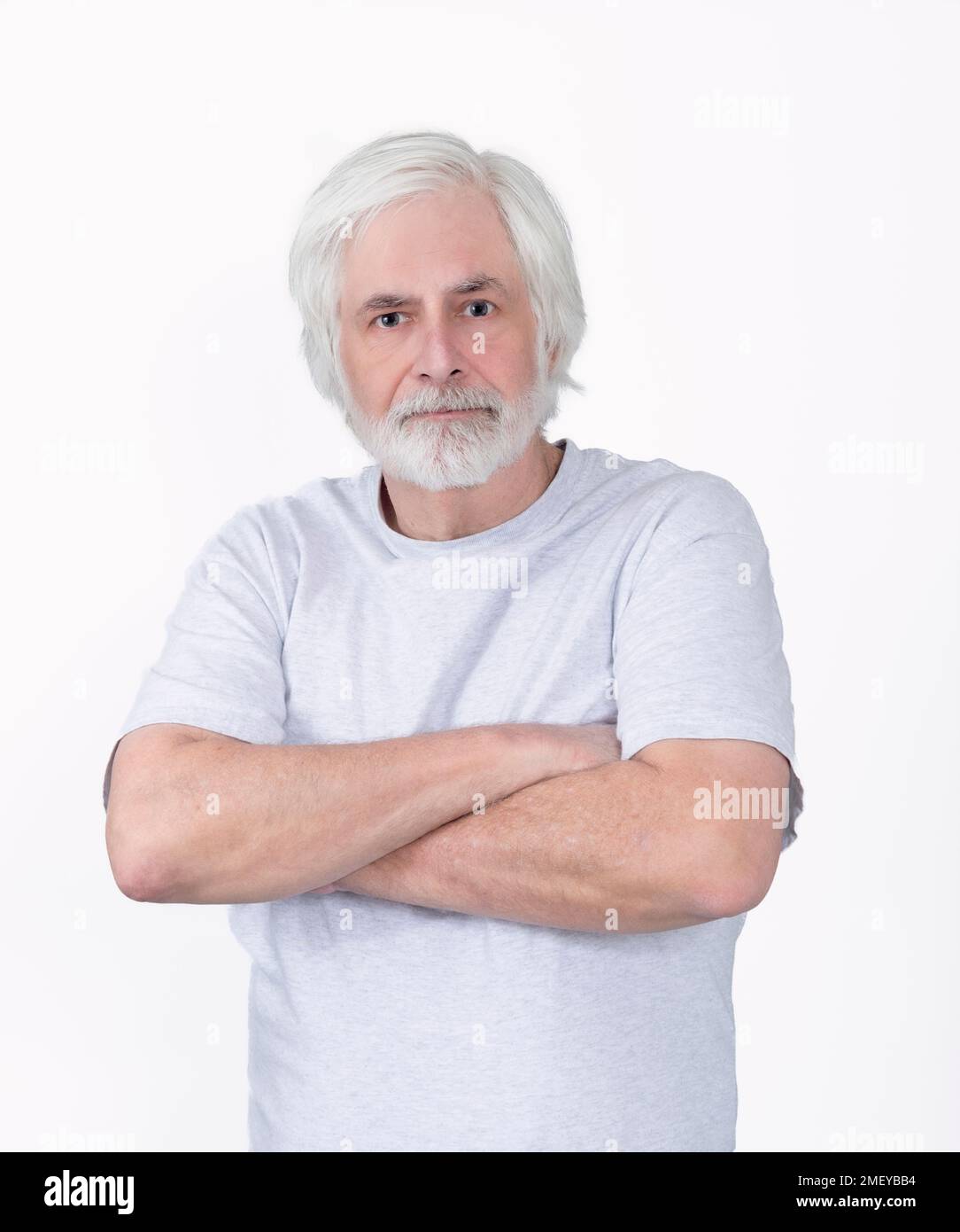 Vertical shot of a scruffy but confident old man with his arms crossed.  Standing from the waist up.  White background. Stock Photo