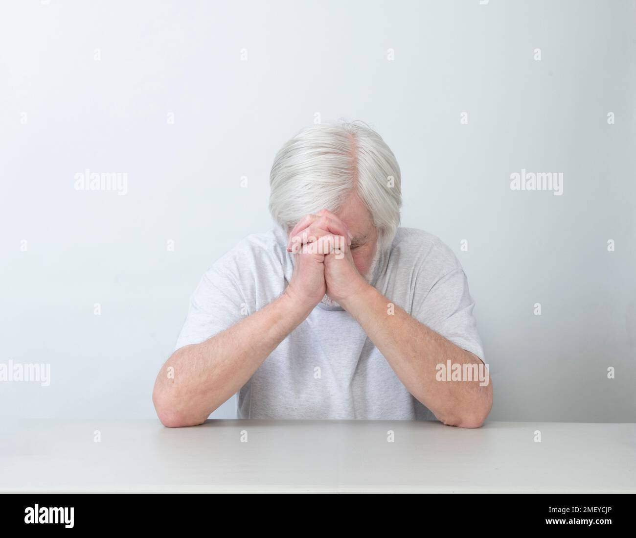 Horizontal shot of a white haired man sitting alone in sadness, prayer or worry.  White background.  Lots of copy space. Stock Photo