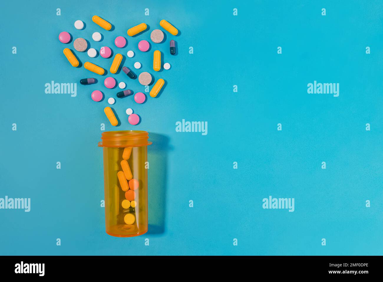 Pills, tablets and capsules arranged in the heart shape, orange bottle on blue background. Medication concept Stock Photo