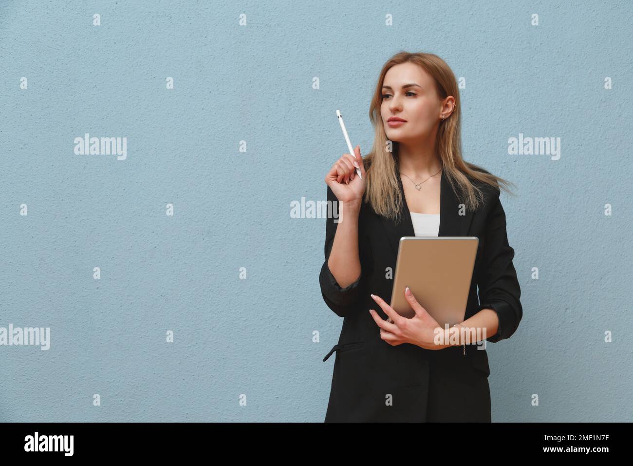 Blonde young business woman wearing black suit over blue plain background, carrying laptop Stock Photo