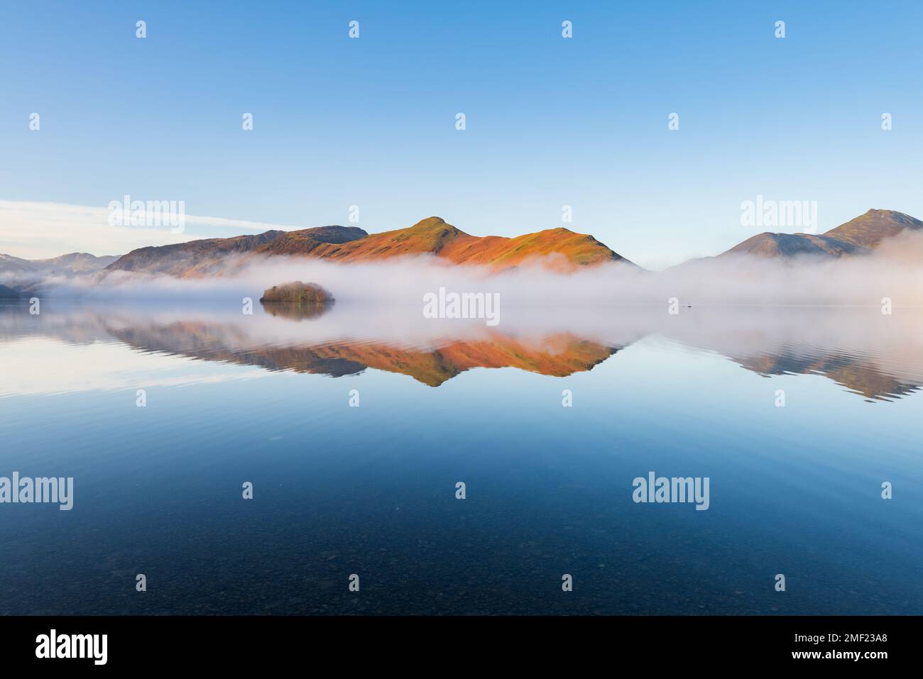 Mirror-like reflections of mountains in misty lake on a sunny blue sky morning. Derwentwater, Lake District, UK. Stock Photo