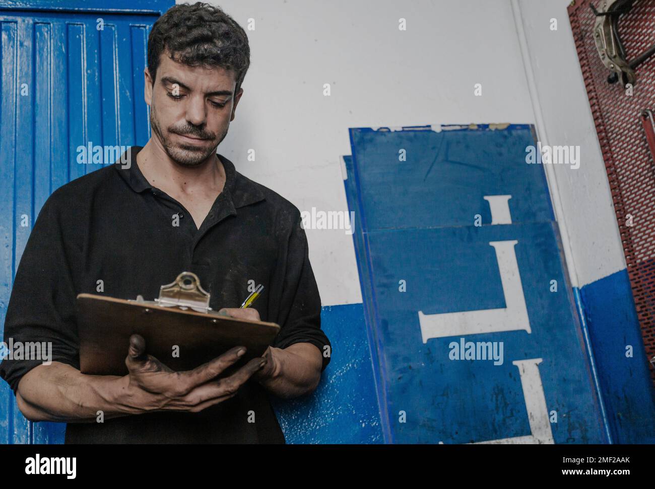 Serious male mechanic in workwear filling in checklist for maintenance and repair service in car station Stock Photo