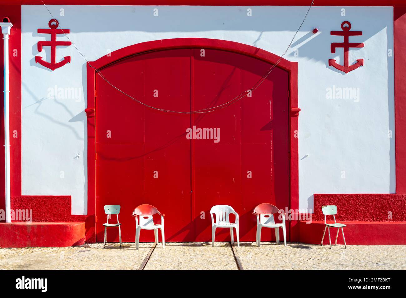 Double red doors and white buiding with chairs outside. old lifeguard station building dating from the 1920s in Alvor, Algarve, Portugal. Stock Photo