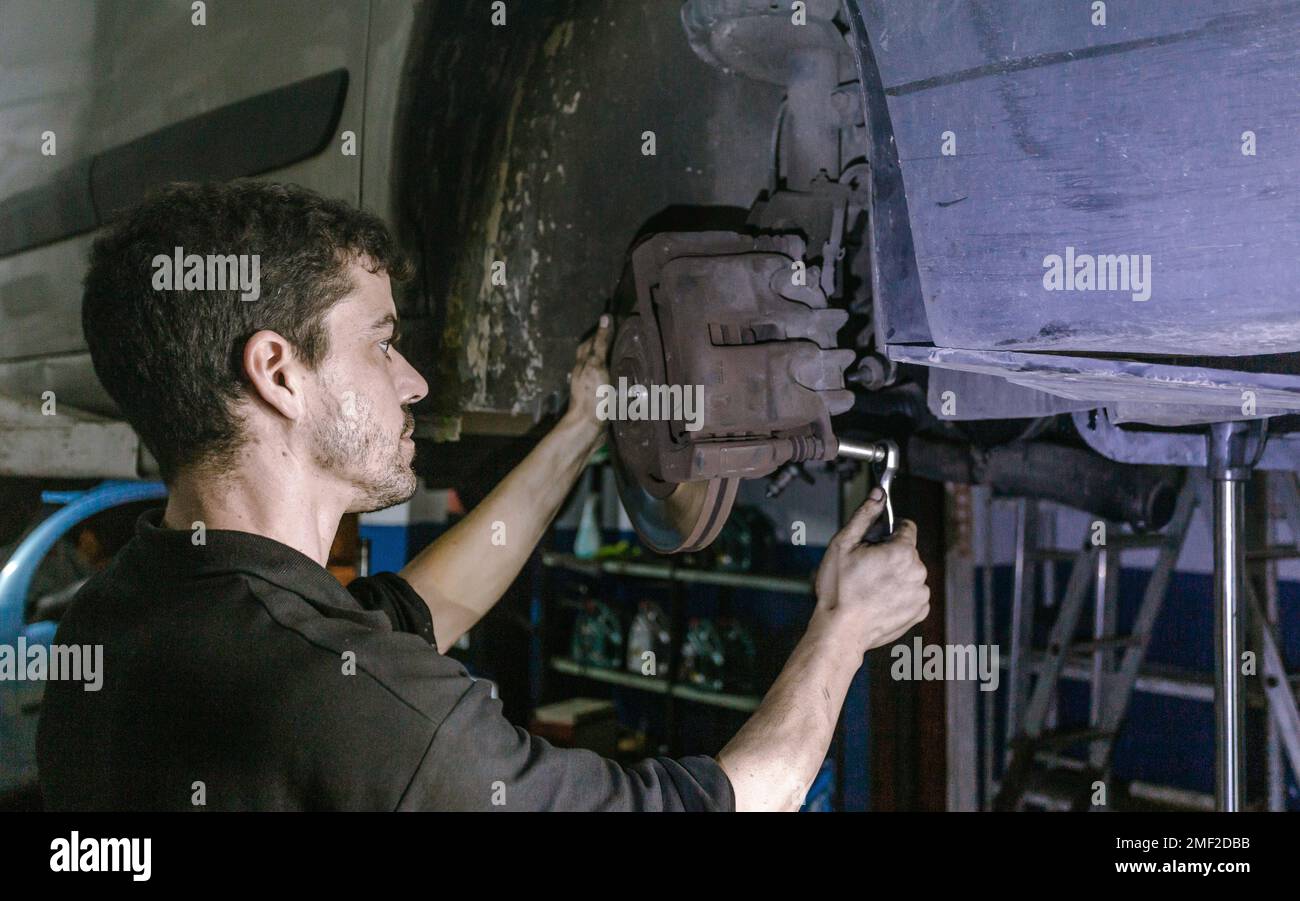 Side view skilled adult male mechanic using ratchet to adjust car brake disc detail while working in garage Stock Photo