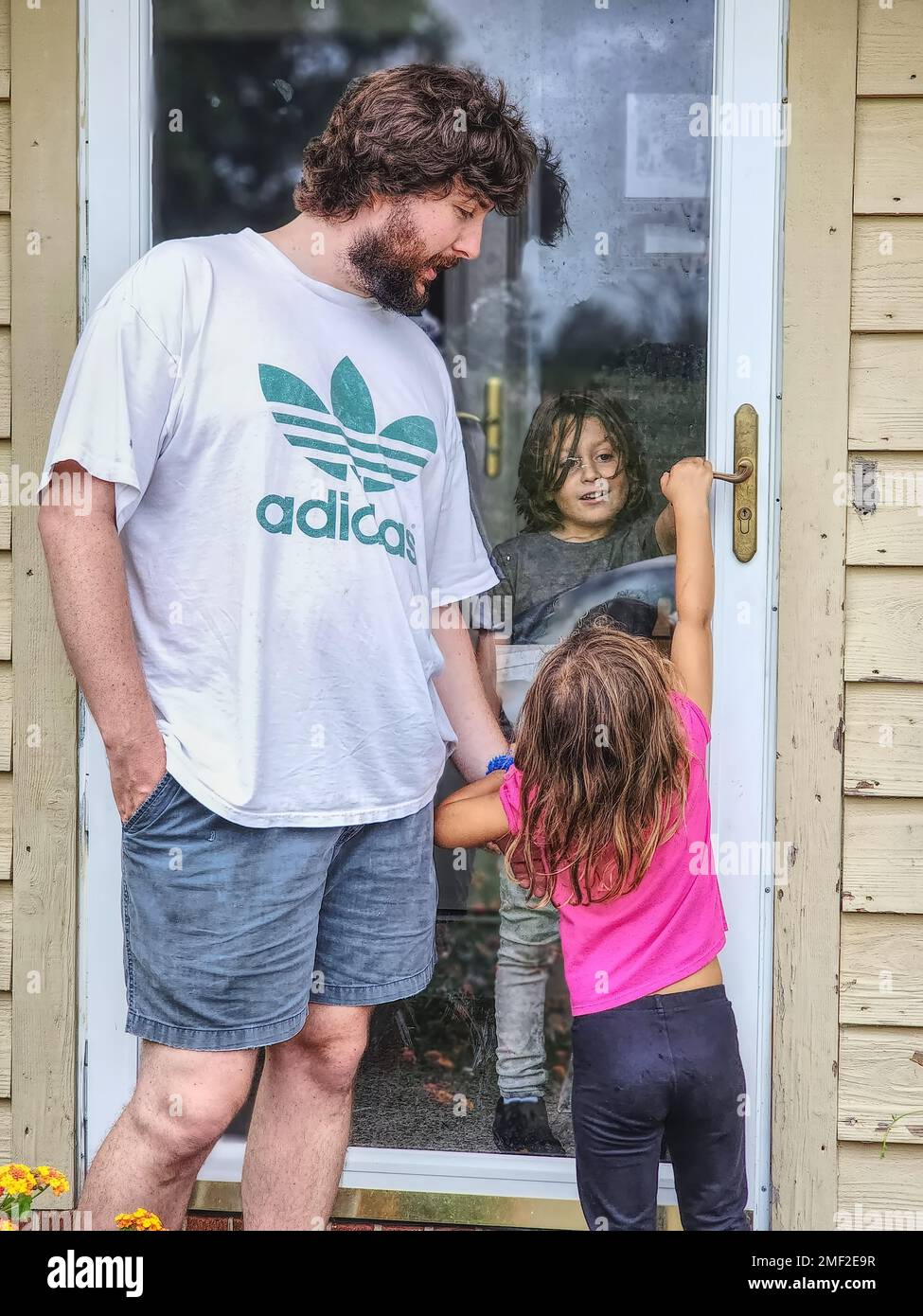 Young man with a little girl outside, near a door with a boy inside Stock Photo