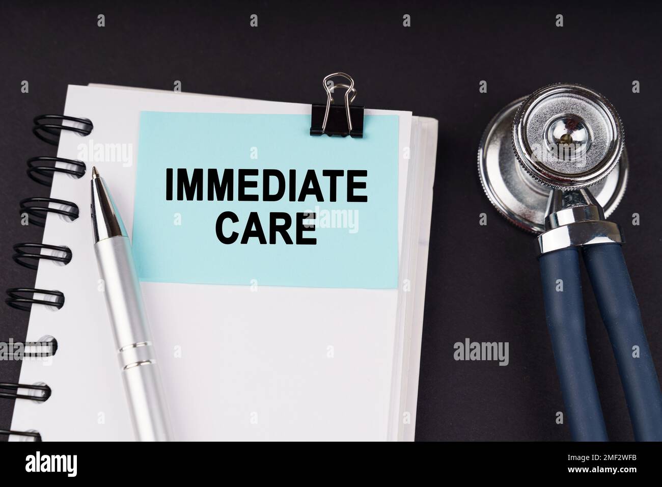 Medical concept. On a black surface, a stethoscope, a notebook, a pen and a blue sticker with the inscription - IMMEDIATE CARE Stock Photo