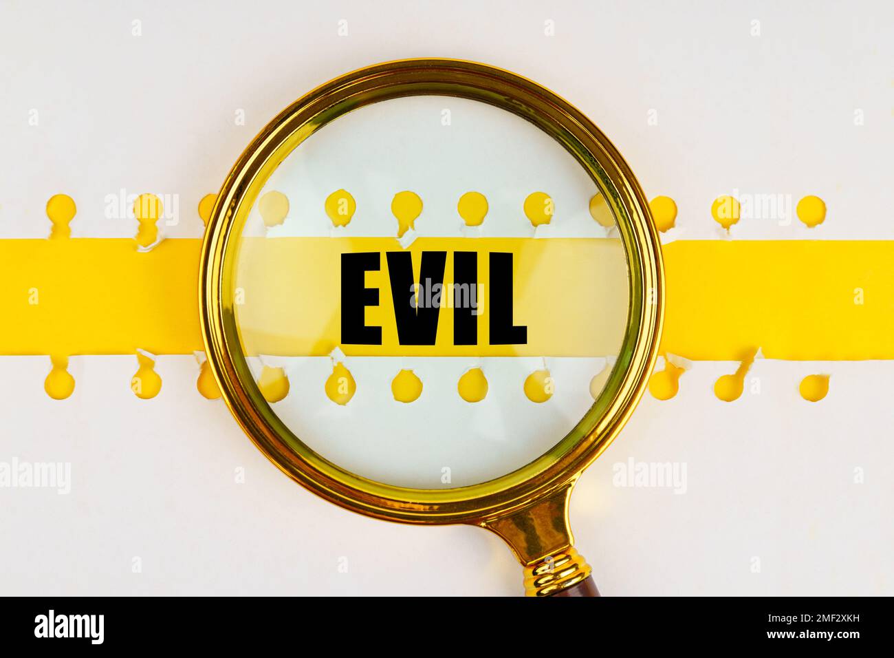 Between two sheets from a notebook on a yellow strip with the inscription - evil, there is a magnifying glass. Stock Photo