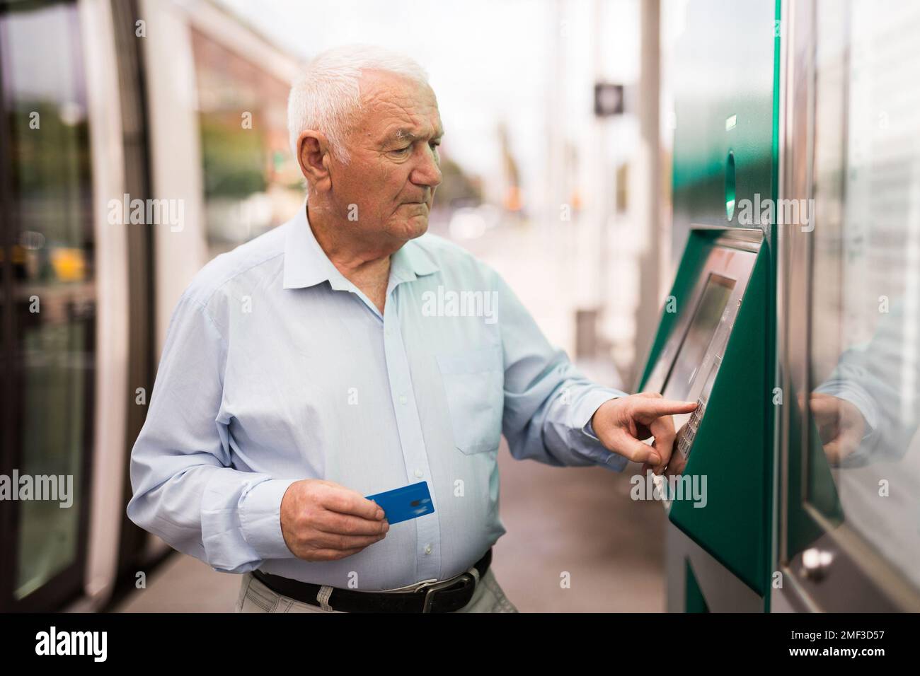 Senior man using ATM machine while standing on tram station Stock Photo