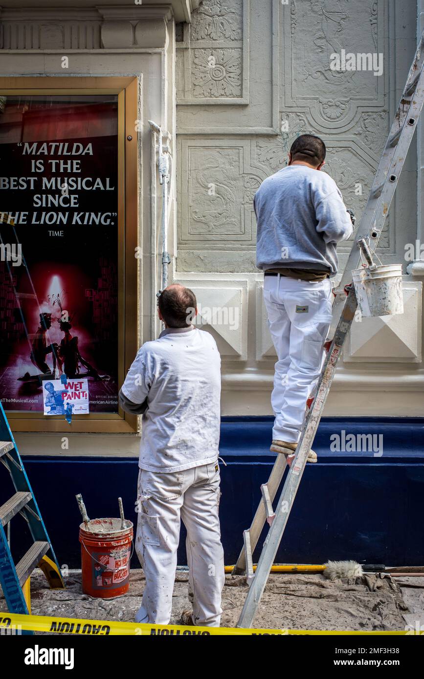 Two people painting exterior of a building using a ladder Stock Photo