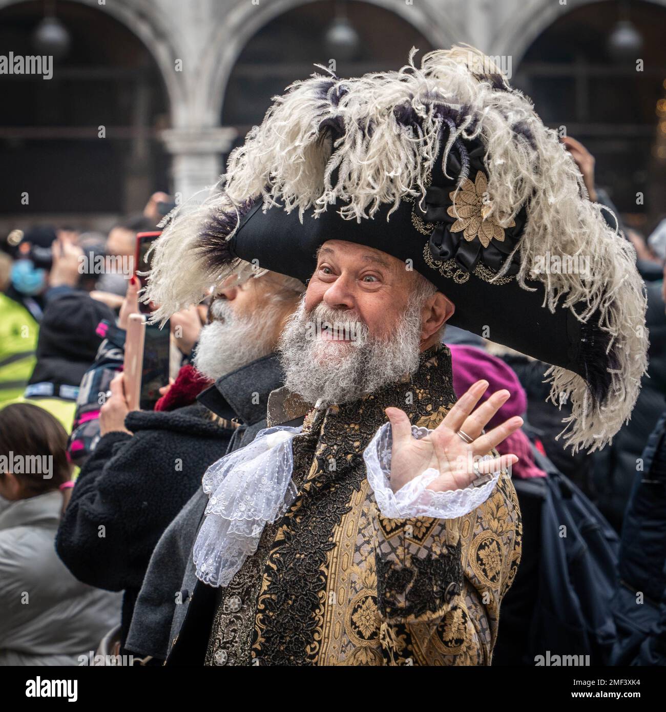 Bearded gray-haired senior man in a big carnival tricorn hat and medieval costume waving hand at the carnival in Venice Stock Photo