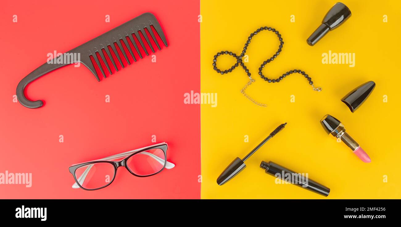 Elegant set of accessory for women. Glasses, cosmetics, jewelry and comb on a yellow and red background.Flat lay,top view. Wide photo. Stock Photo