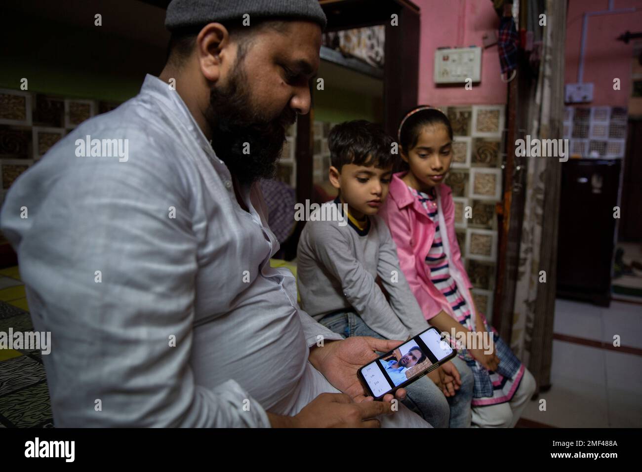 Haroon, holds a mobile phone as his nephew and niece look at the ...