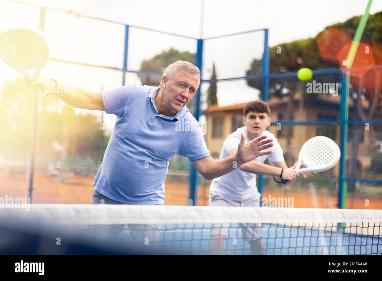 concentrated elderly woman padel player hitting ball with a racket on 
