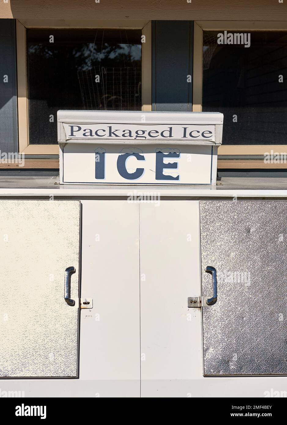 A white and stainless steel commercial bagged ice cube freezer stands outside a convenience store. Stock Photo