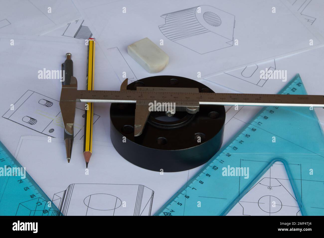 Image of a mechanical part and a precision measuring caliper resting on blueprints. Mechanical engineering works and drawings. Stock Photo