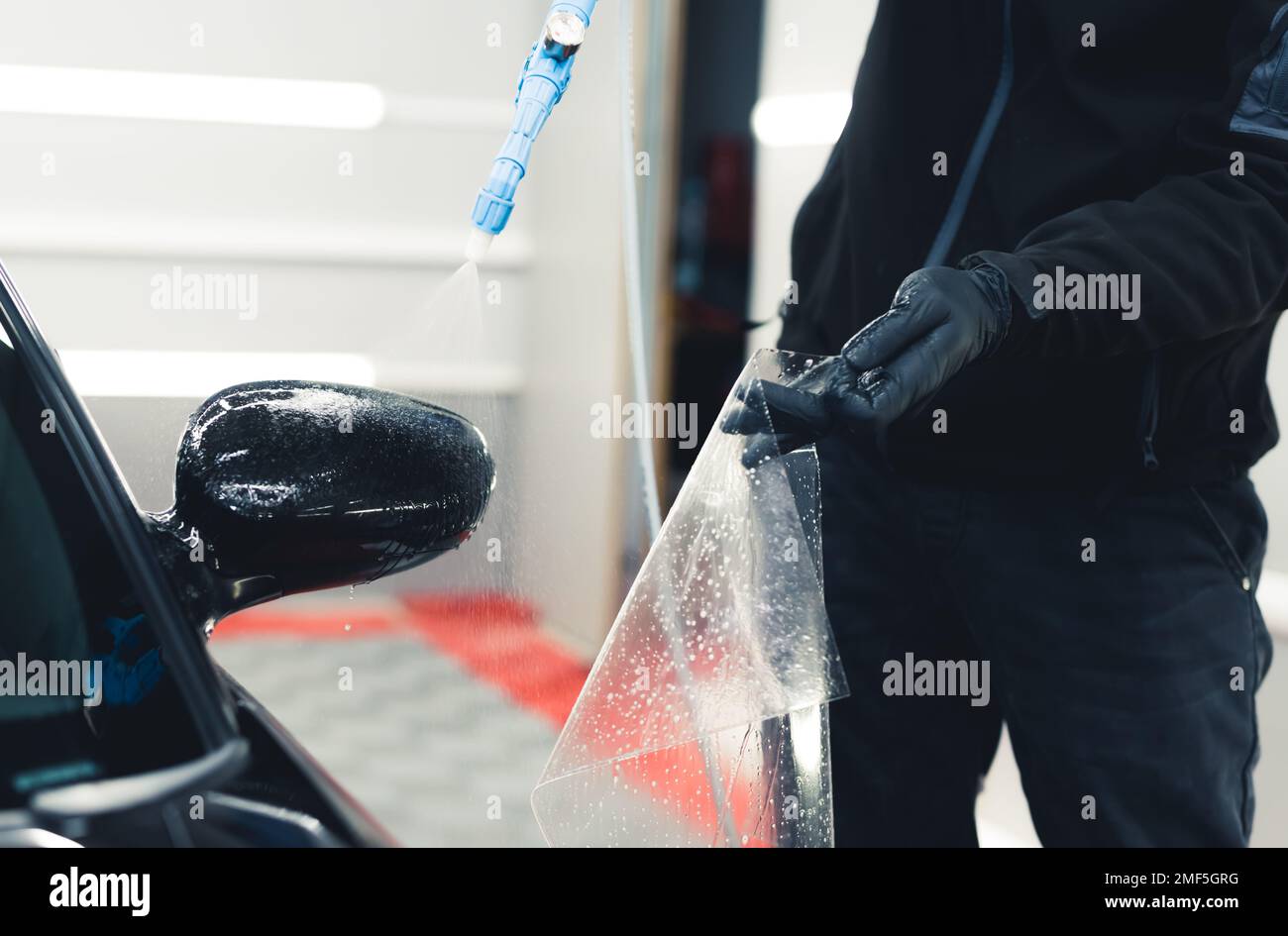 Unrecognisable man wearing black gloves spraying side mirror of car