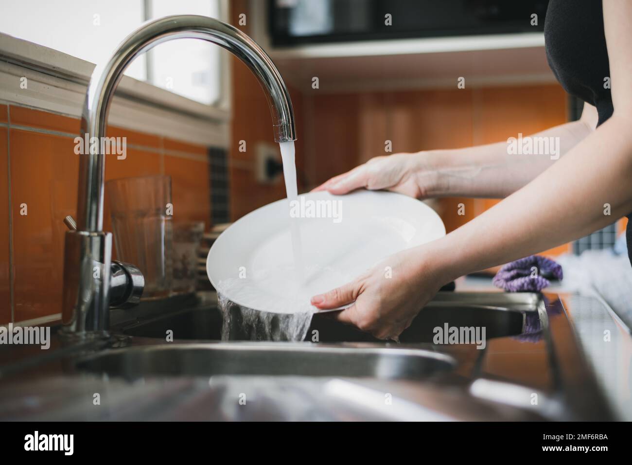 Woman washing dishes in kitchen sink, close up of hands rinsing plate. Stock Photo