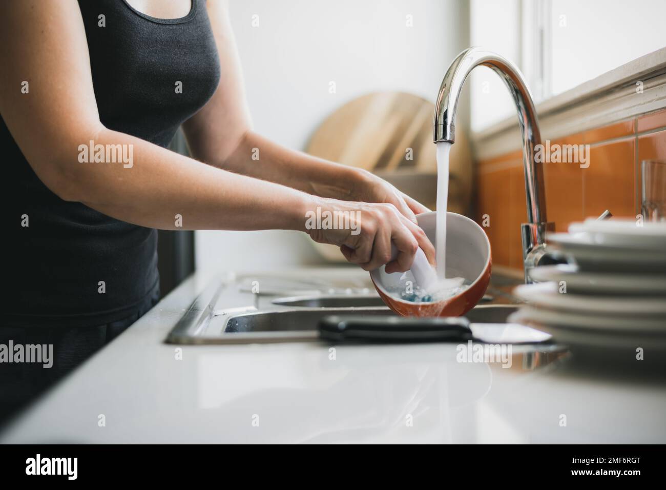 Woman washing dishes in kitchen sink, close up of hands and scrubbing brush with water running Stock Photo