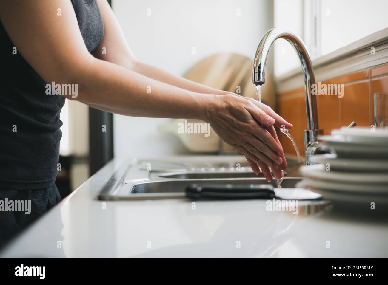 Woman washing hands in kitchen sink, close up of hands with water running. Stock Photo