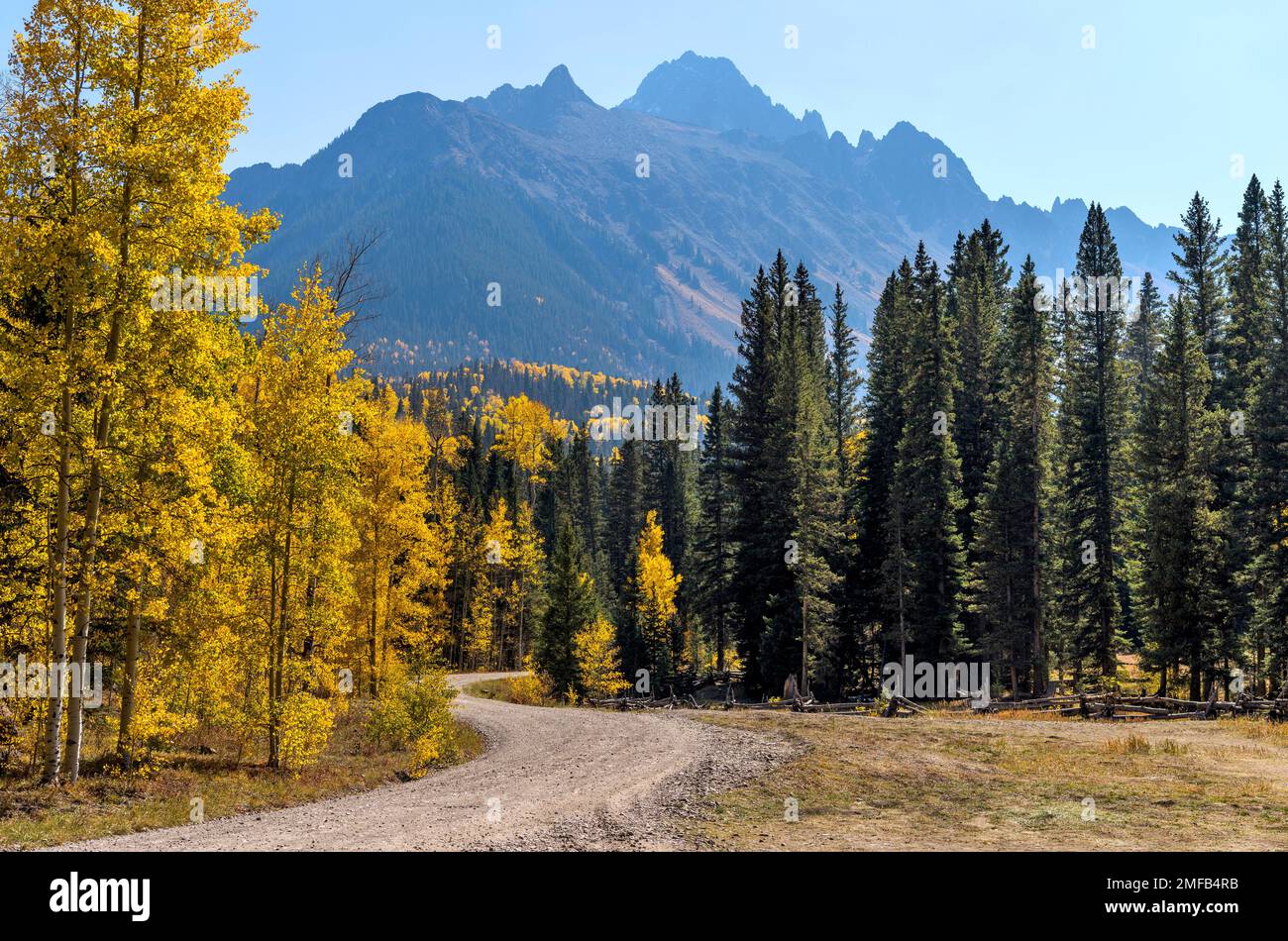 Autumn Mountain Road - A backcountry road winding  in a colorful valley at base of rugged Sneffels Range on a sunny October afternoon. Ridgway, CO, US. Stock Photo