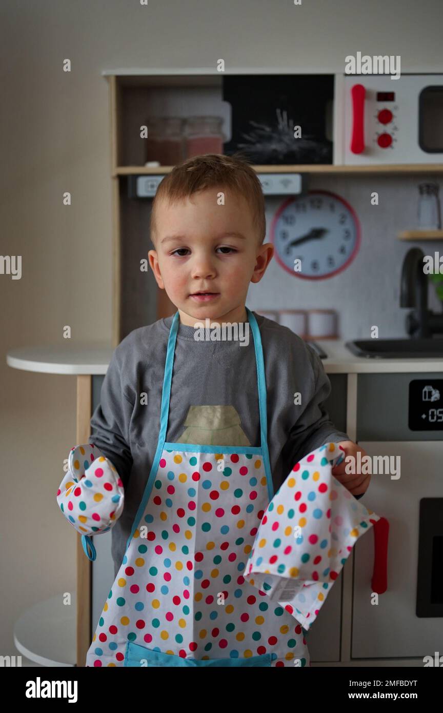 Cute little toddler with apron and glove standing in front of toy
