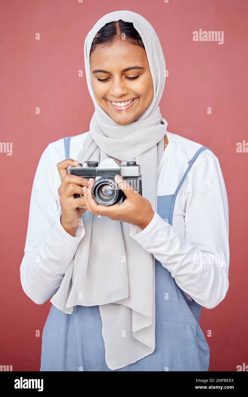 Muslim, hijab and photographer shooting a picture or photo with a retro camera isolated in a studio red background. Islam, Dubai and woman in scarf Stock Photo