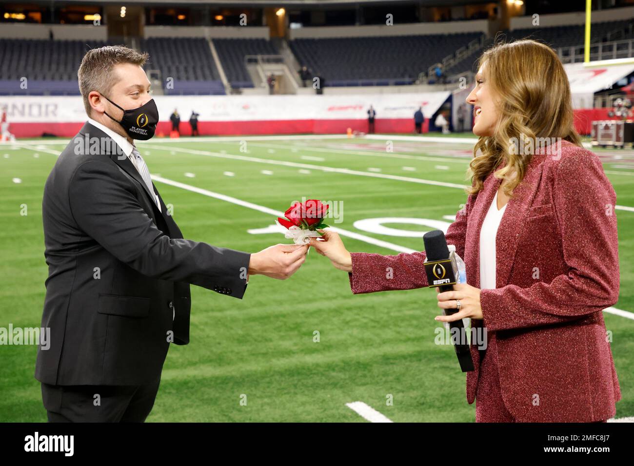 Jason Martin, left, hands roses to ESPN sideline reporter Allison Williams,  right, on the field at AT&T Stadium before the Rose Bowl NCAA college  football game between Notre Dame and Alabama in